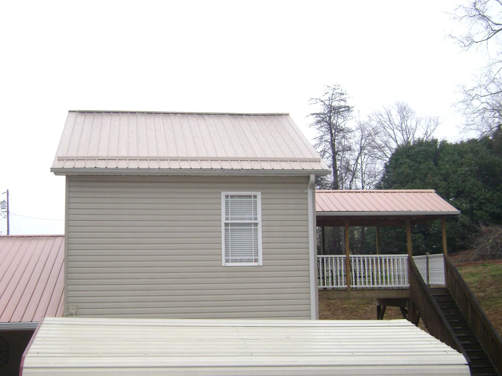 Tan metal roofs on a two story addition and attached porch, from a Roof Replacement job in Miami